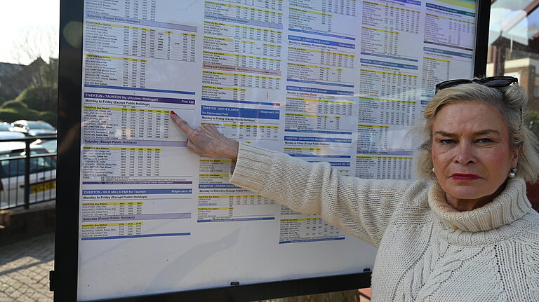 Rachel Gilmour stood in front of a bus timetable, pointing and looking angry